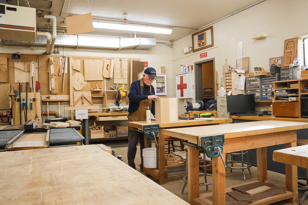 Man works in woodshop full of benches and many materials