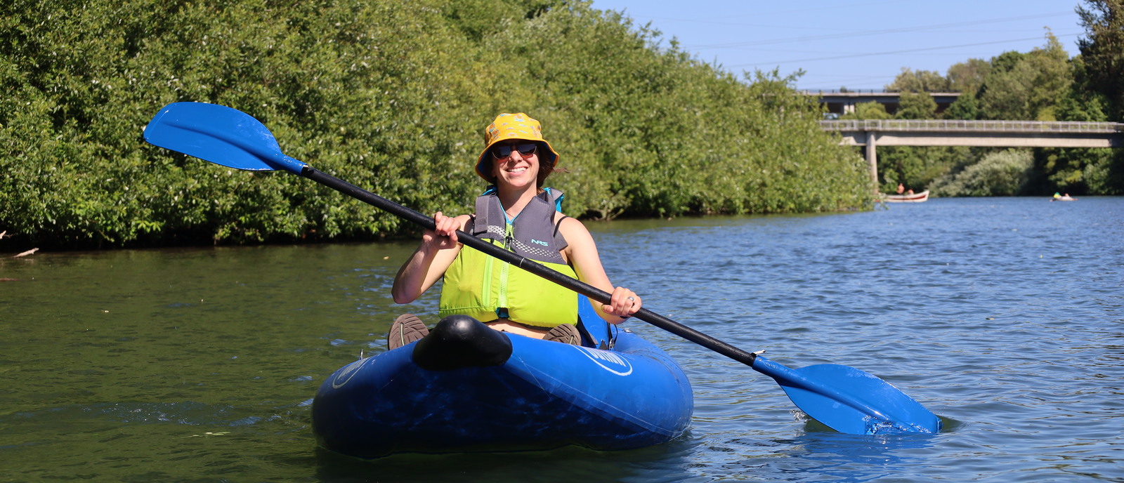 A person paddles an inflatable kayak on a sunny day