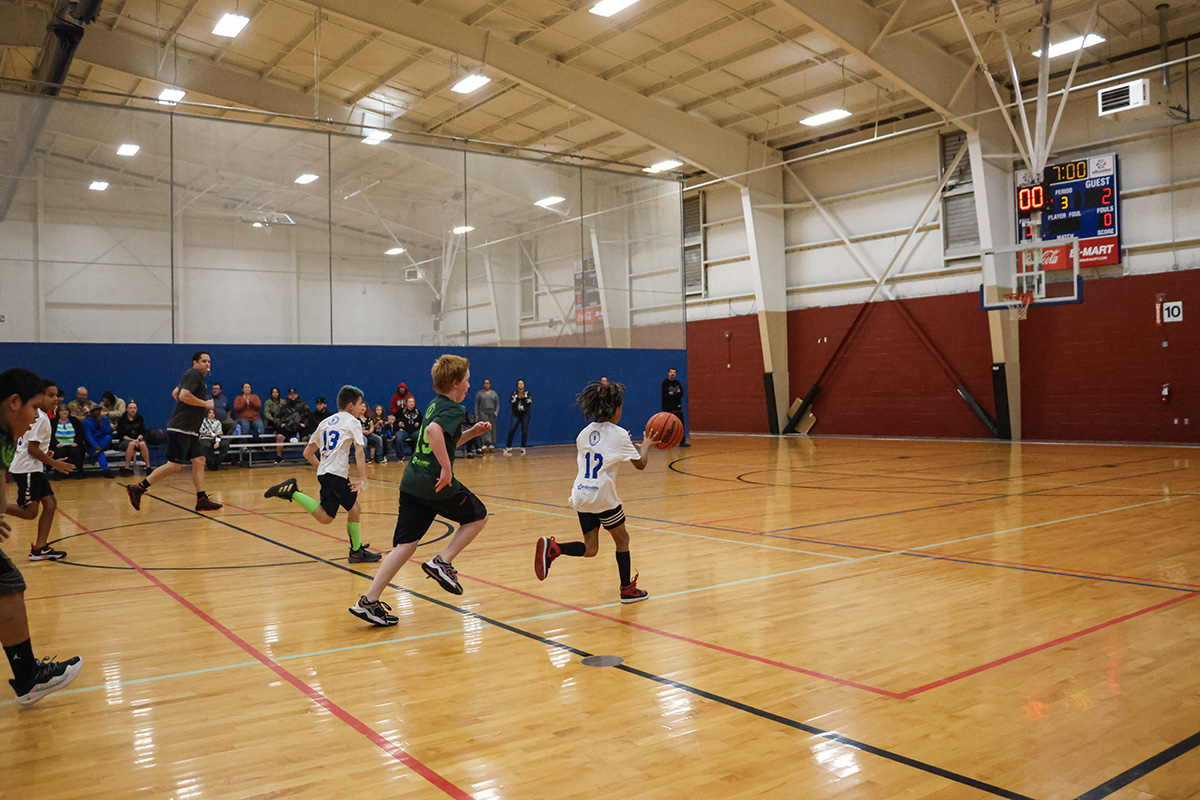 Kids playing in basketball game wearing jerseys and running toward a hoop