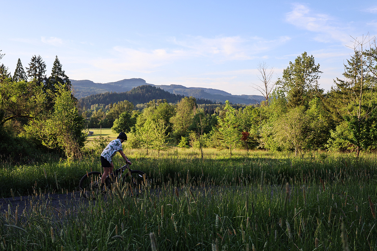 Woman on mountain bike riding on a path on a sunny day with trees and mountains in the background