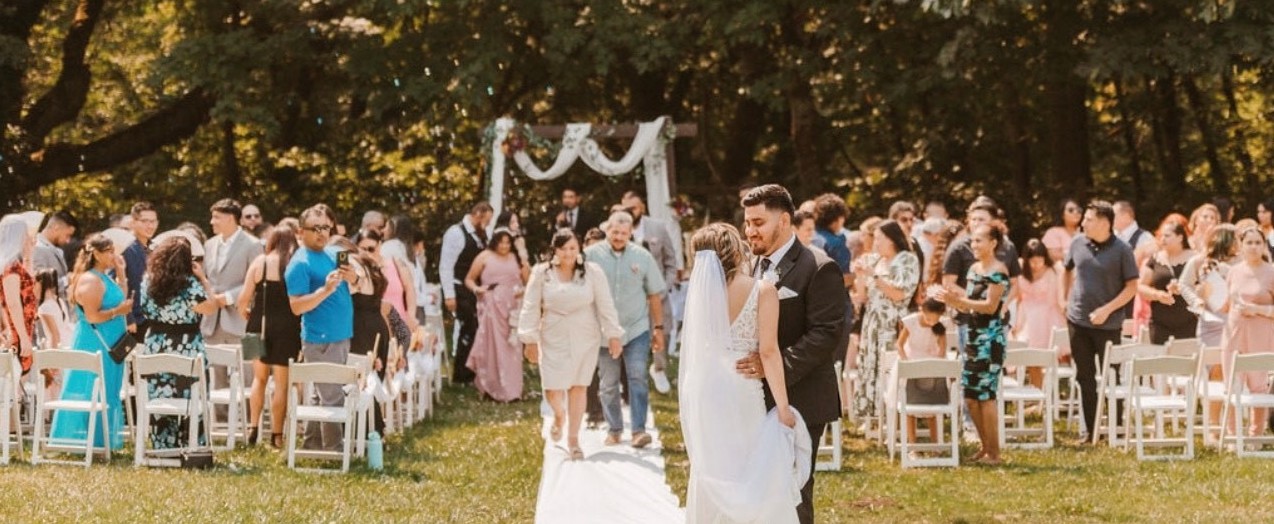 A bride and groom stand in front of their guests at an outdoor wedding