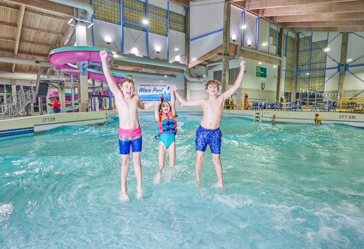 Three kids jumping in the water at an indoor pool.