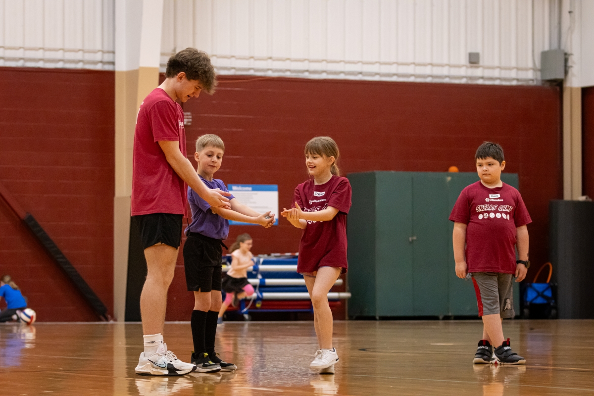 Coach demonstrating and teaching children proper form on a gym floor.
