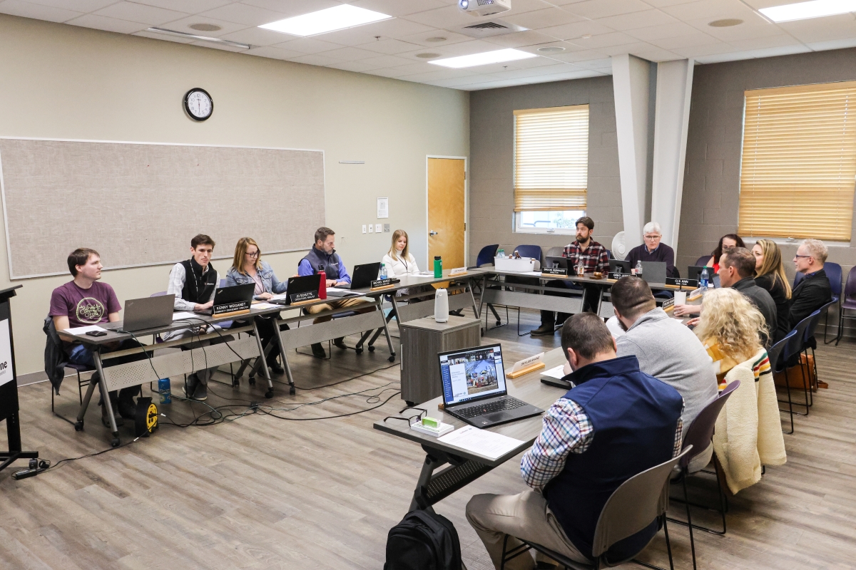 A group of adults sitting at tables in a u-shape, having a meeting and talking to each other.