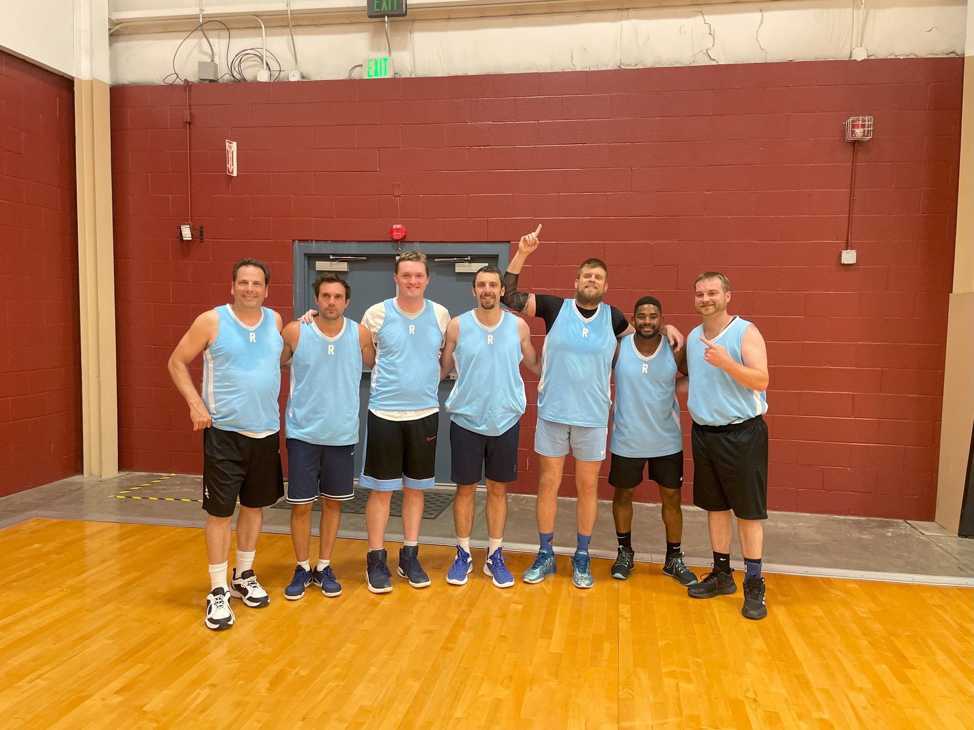 Seven men in matching blue jerseys smiling in the gym
