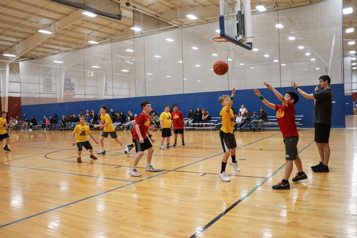 Two basketball teams in red and yellow jerseys toss a ball in the air at an indoor court.