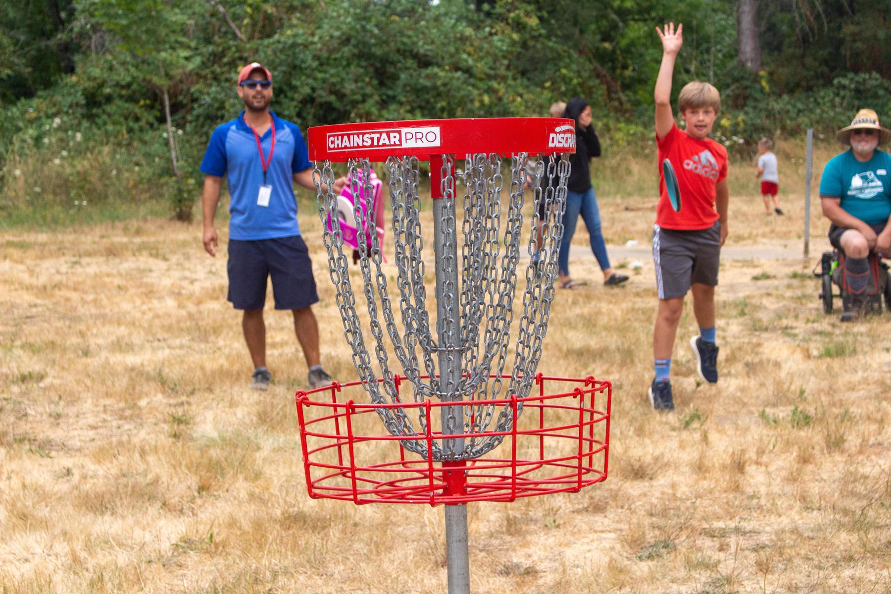 Kids throw discs at disc golf basket