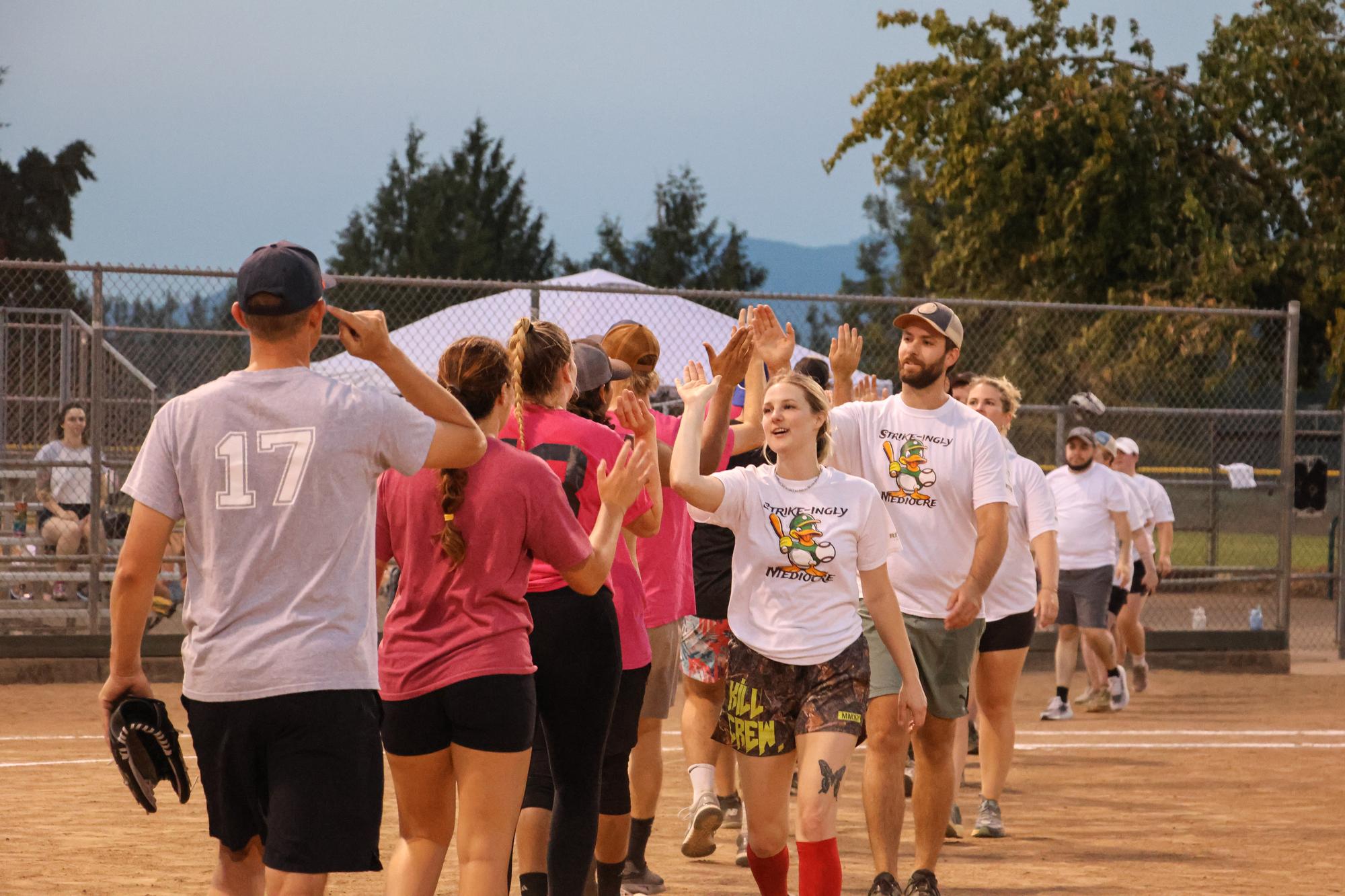 two softball teams walk past eachother giving high-fives after the game