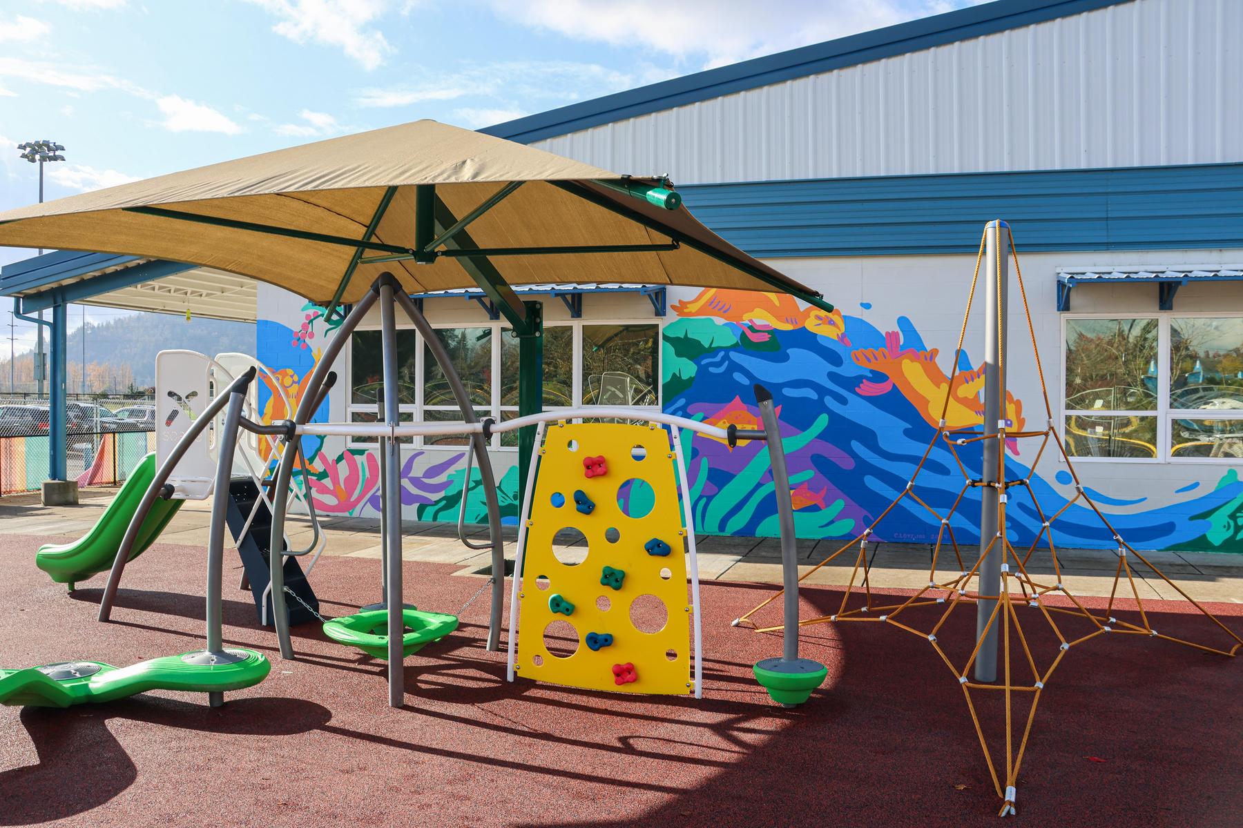 New playground equipment sits on a sunny day in front of duck-themed mural