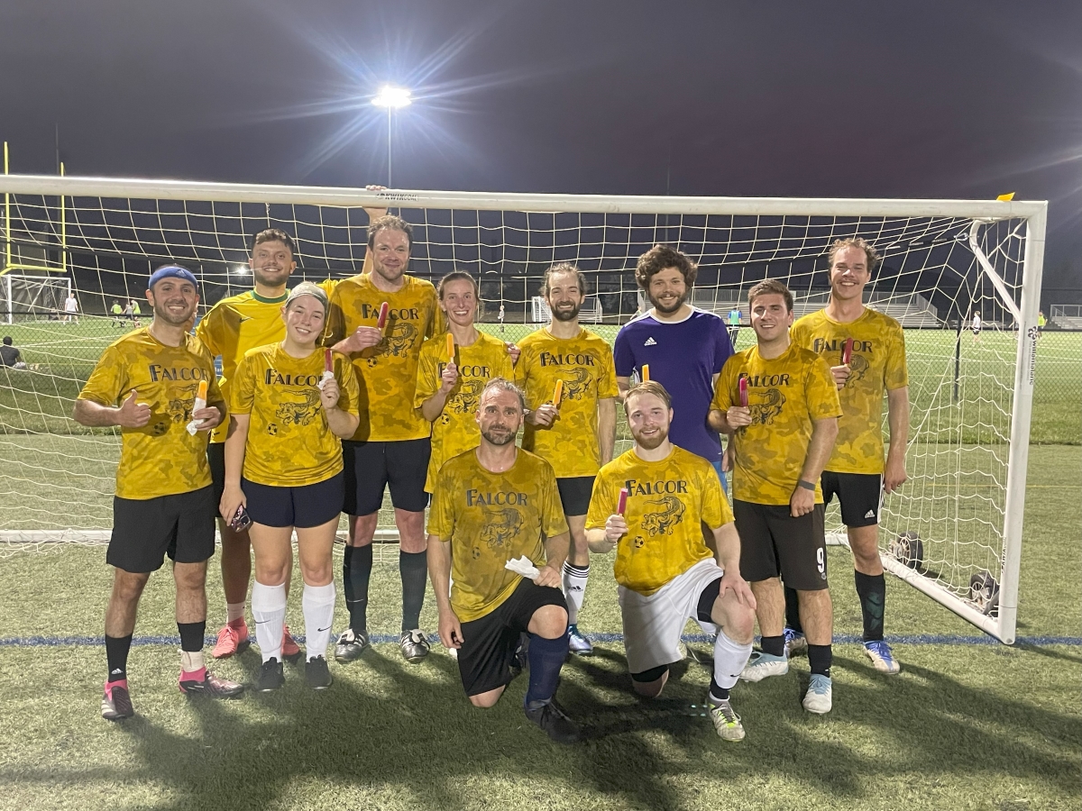 A soccer team wearing yellow jerseys poses on a turf field under bright lights after a night game.