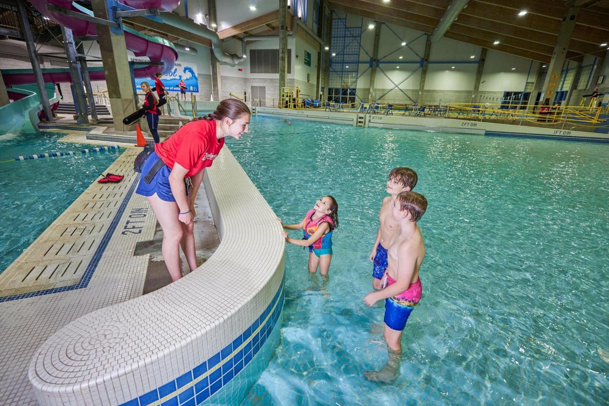 Three children talk to lifeguard while standing in the wave pool