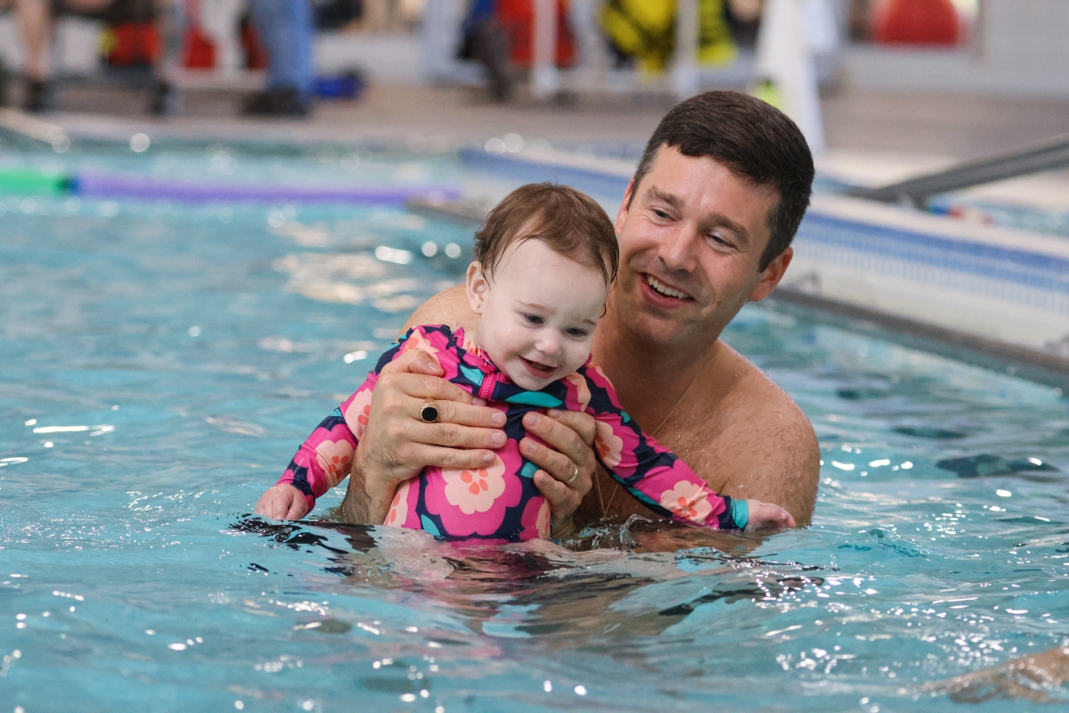 A young child in a pink swimsuit is held up in the water by an adult while learning to swim.