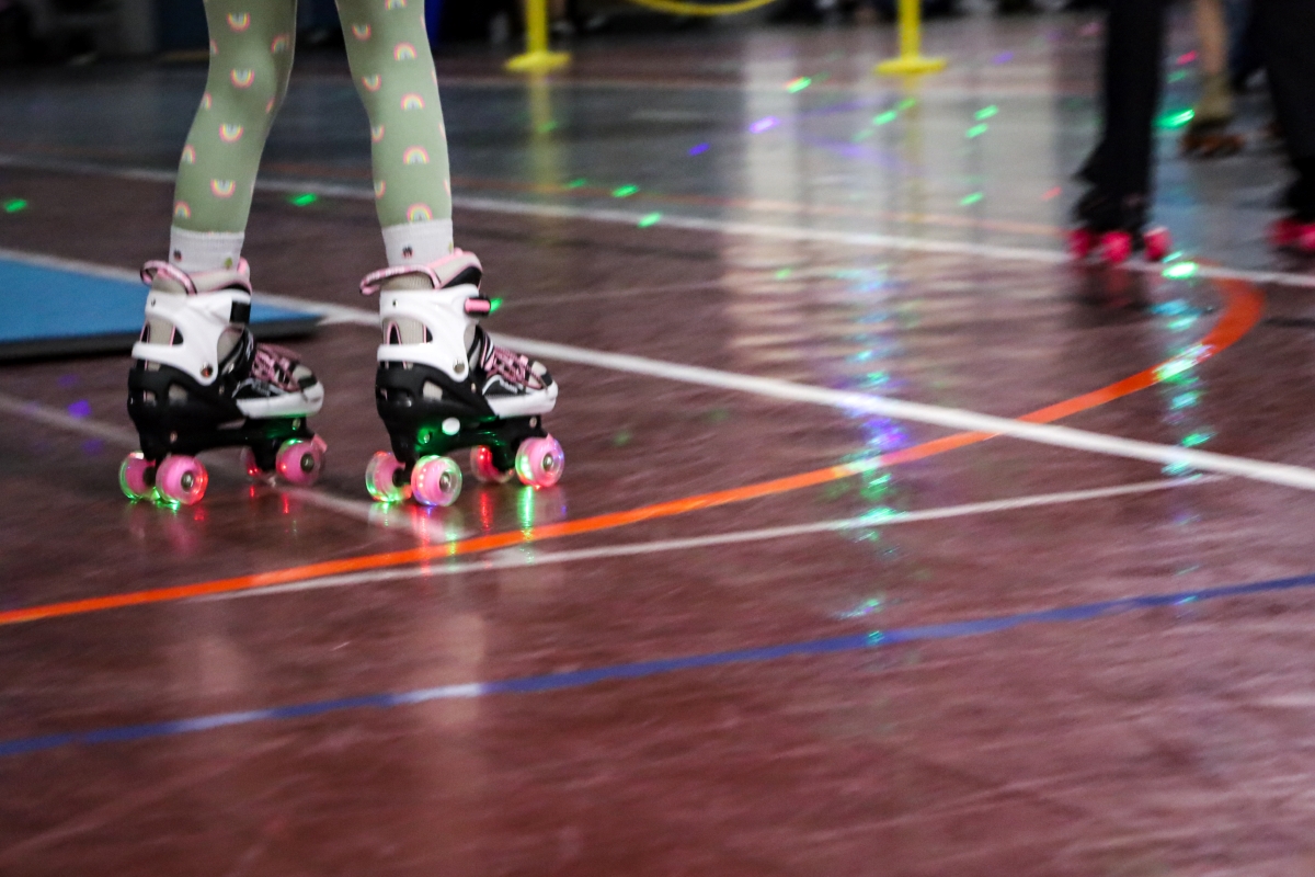 A pair of rollerskates with glowing lights on the wheels glides on top of a brown floor.