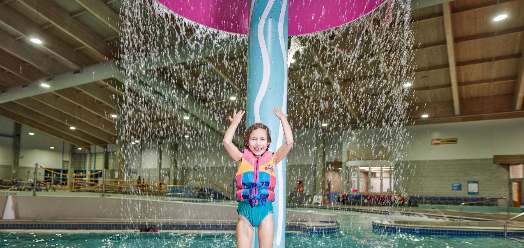 Child stands under jellyfish waterfall at indoor pool