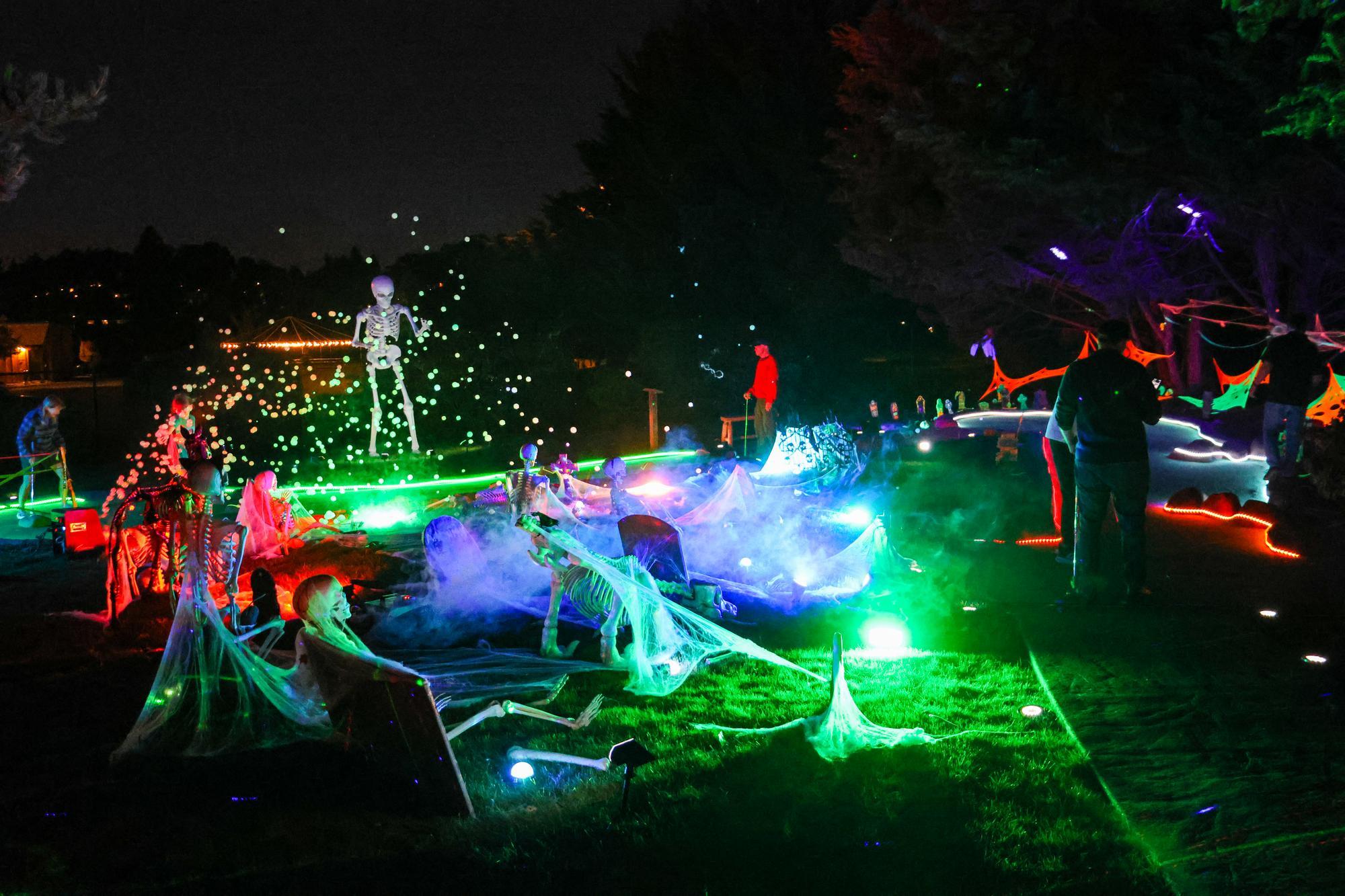 Glowing colorful lights illuminate a mini golf course at night with halloween decorations.