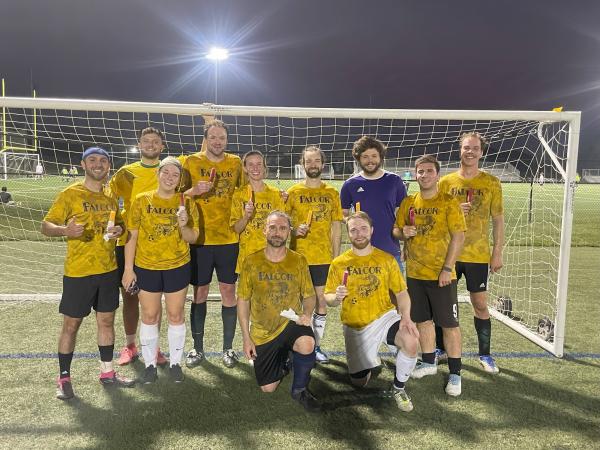 eleven soccer players pose infront of a soccer net wearing matching yellow jerseys