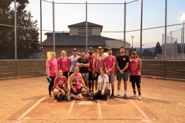 twelve softball players pose at home base wearing pink shirts