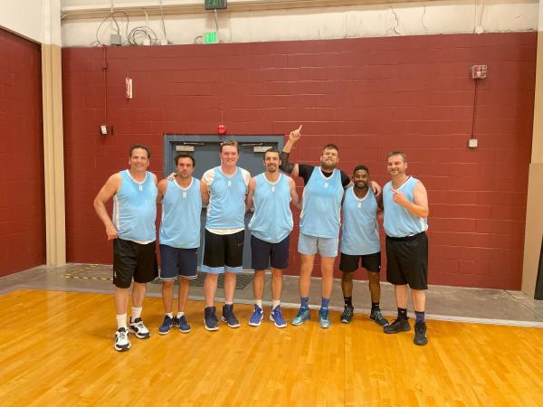 Seven men in matching blue jerseys smile in the gym