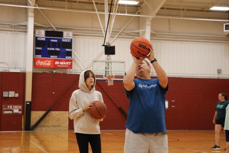 An adult holds up a basketball, showing a teen proper throwing technique