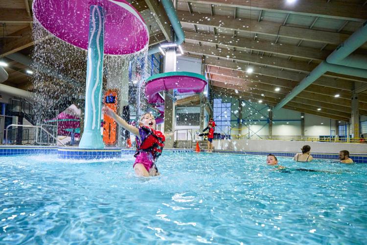 Young child wearing lifejacket plays near jellyfish water fountain at the pool