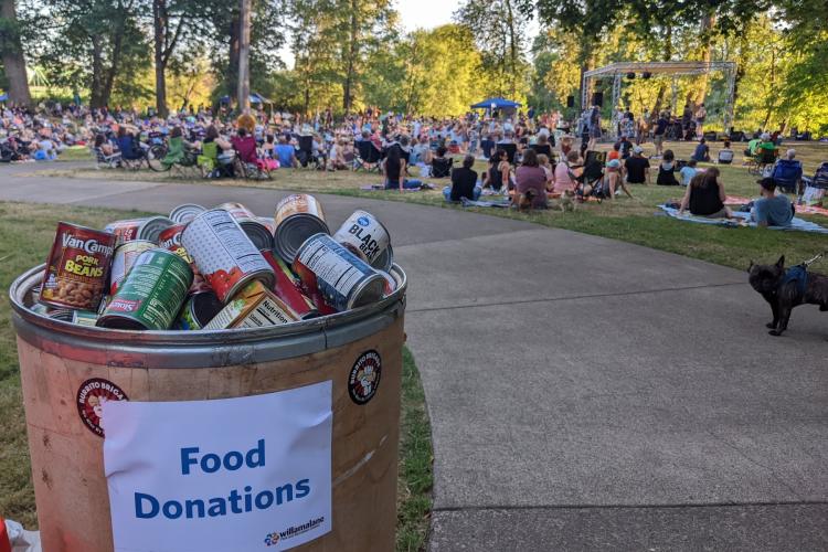 A food donation bin is full of canned food at an outdoor concert event