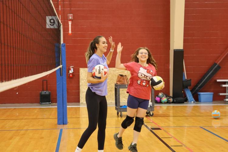 A coach high-fives a volleyball player on the court.