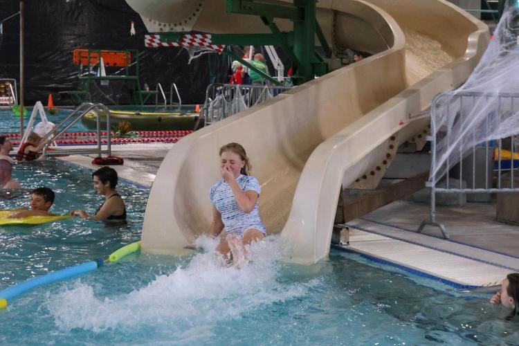 A teenager floats down a waterslide, splashing into the pool below.