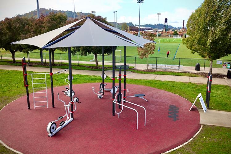 An outdoor, shaded area with fitness equipment near sports fields