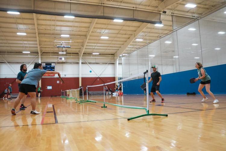 Four people stand on both sides of a short net on a wood court.