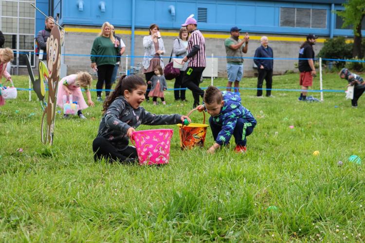 Kids drop eggs into buckets during group outdoor egg hunt