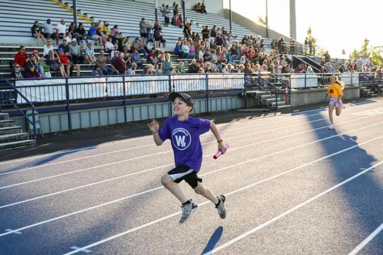 A young athlete sprints on a blue outdoor track.