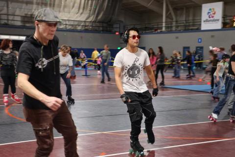 Two adults skate in a packed gym.
