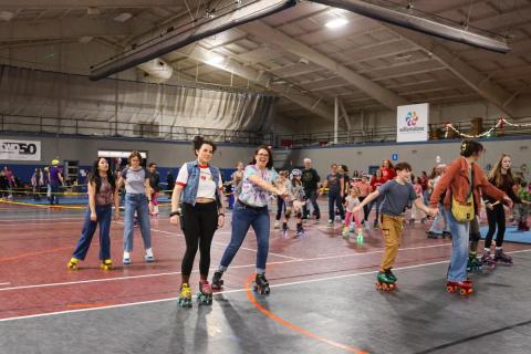 A group of people skate on the gym floor with their arms outstretched.