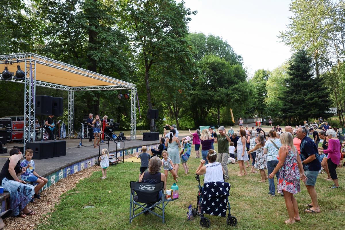 A group of people dancing on a green lawn in front of a stage with live music playing.