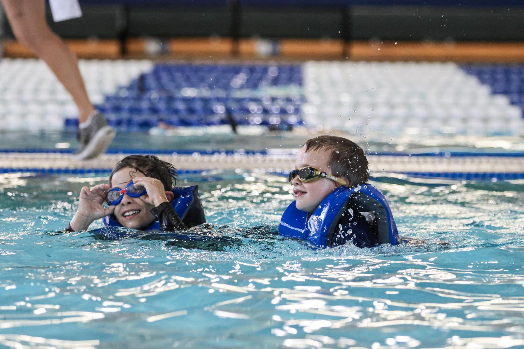 Two kids swim with lifejackets and goggles