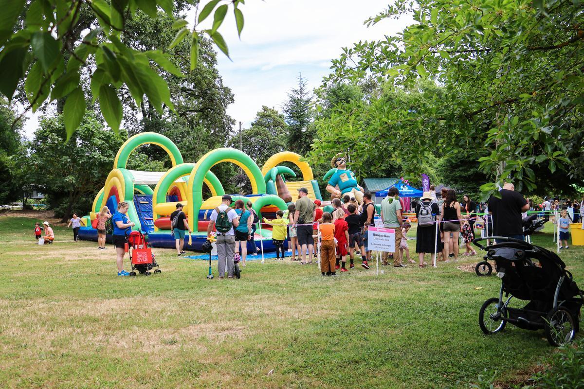 A group of people stand next to colorful bounce houses, sitting on green grass.
