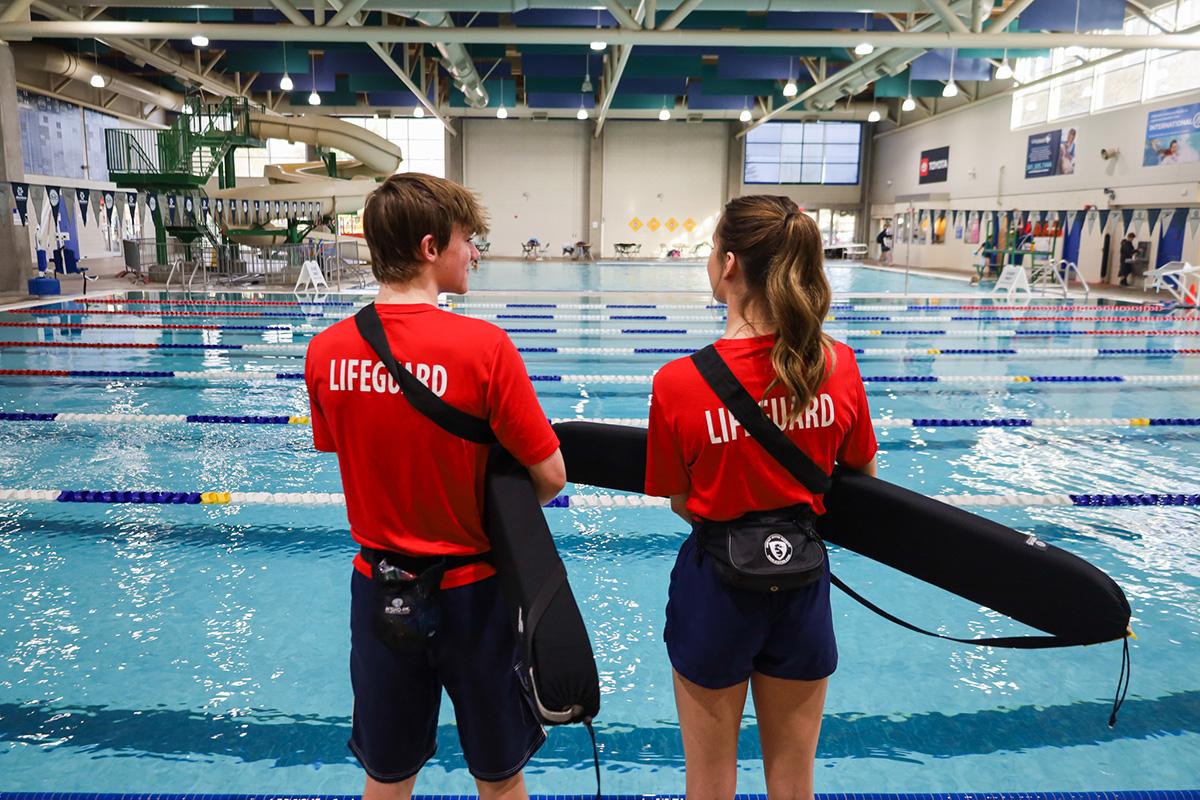 Two young lifeguards monitor a lap swimming pool indoors