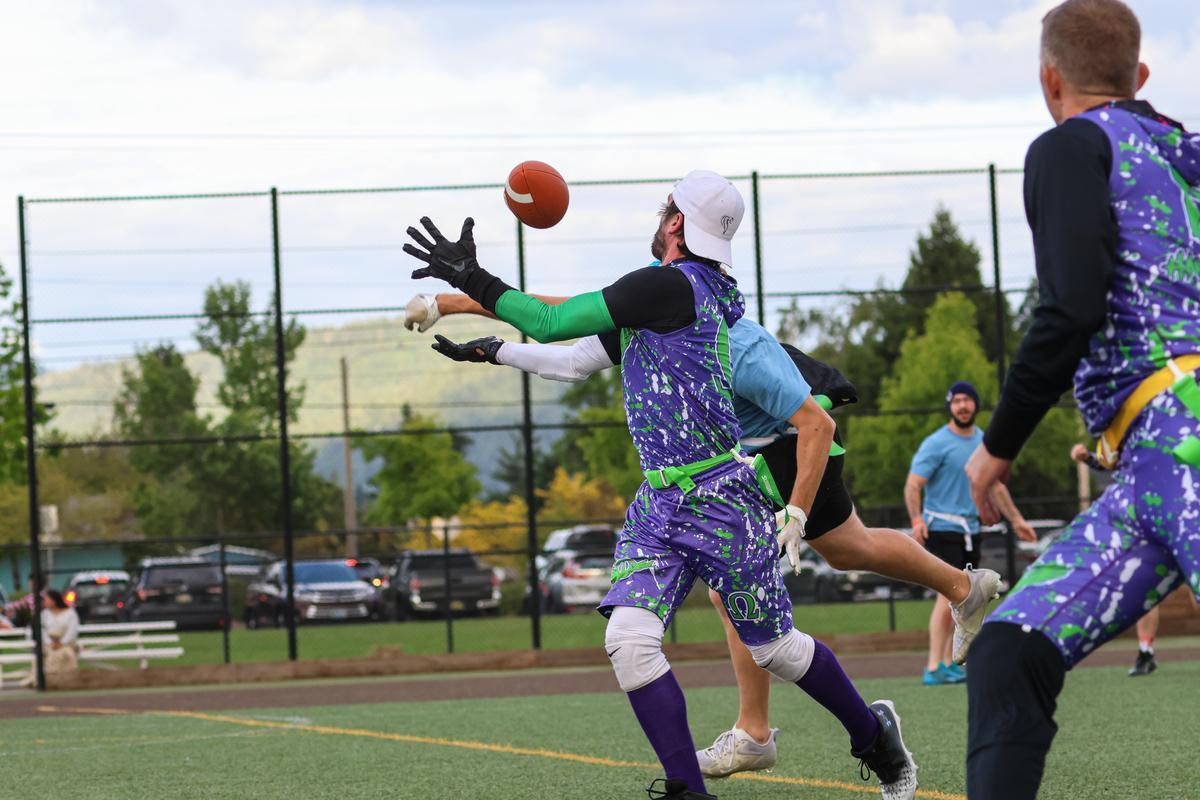 An adult in a yellow and green jersey reaches their arms out to catch a football.