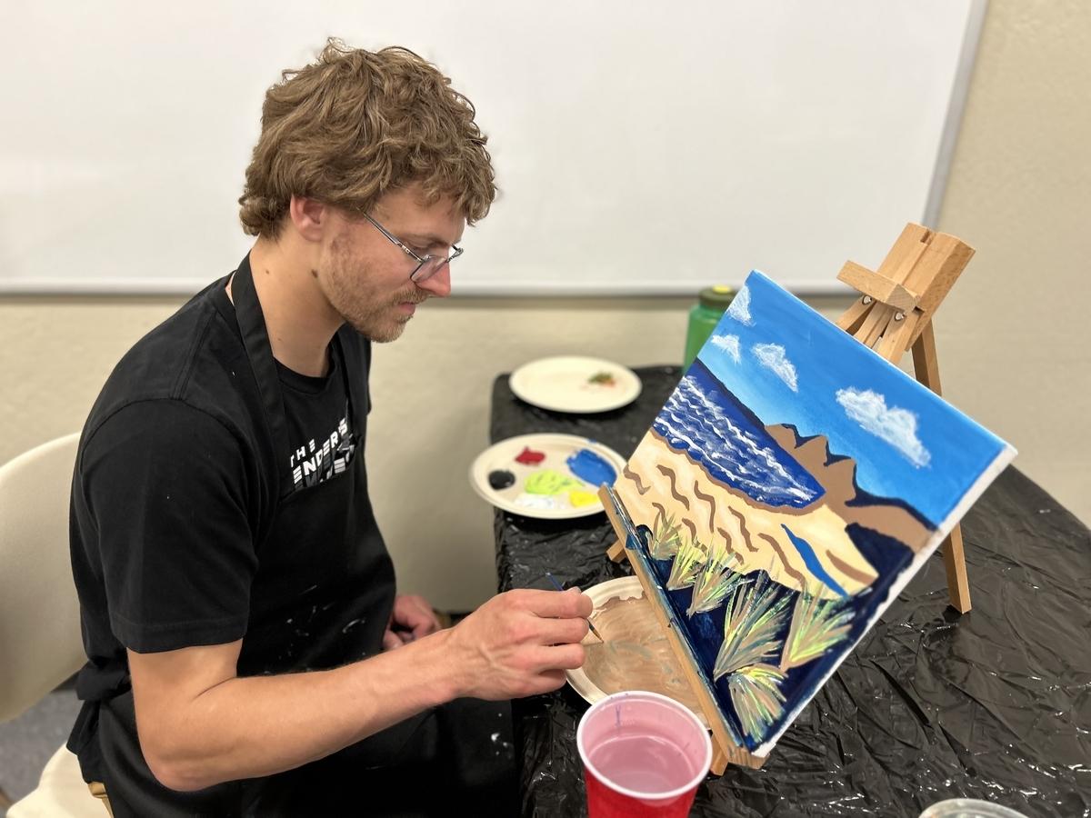 An adult looks toward a painted canvas with a blue beach scene.