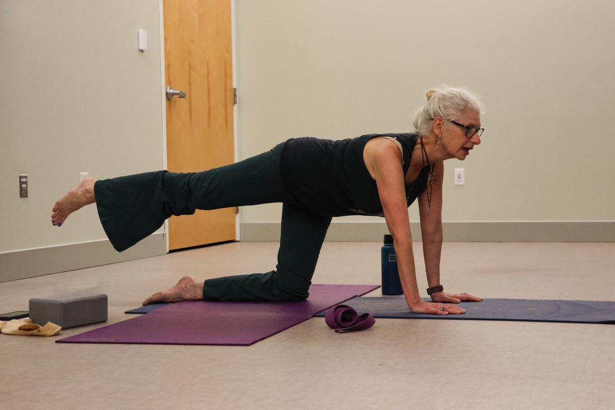 An adult does a yoga pose on their hands and one knee on the floor.