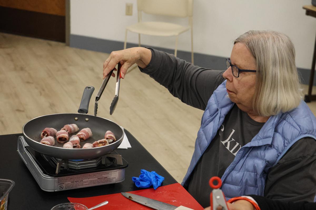 An adult flips food in a hot pan with a pair of kitchen tongs.