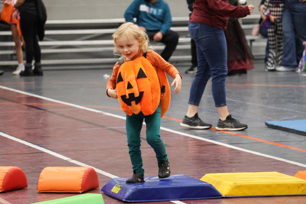 A child wearing a pumpkin costume hops over agility pads.