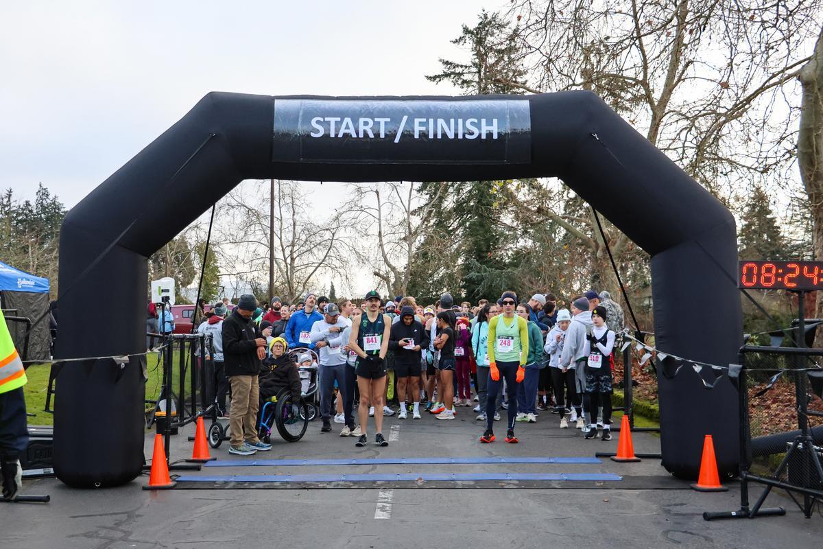 A crowd of people stand behind a black starting arch before a 5K.