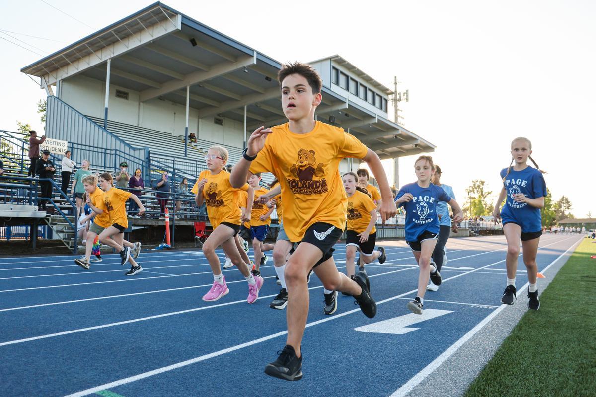 A kid in a yellow shirt sprints ahead of the group on the track.