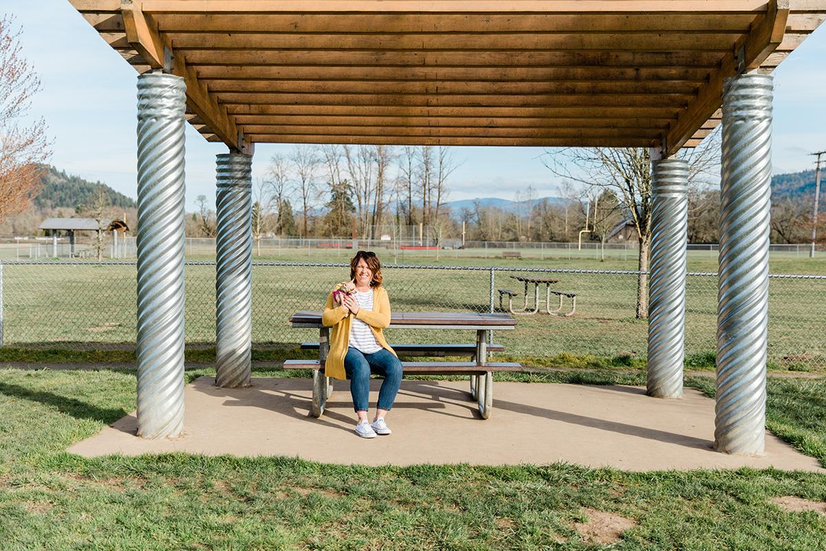 A woman sits with her small dog under the shelter and at a picnic table at the Willamalane dog park