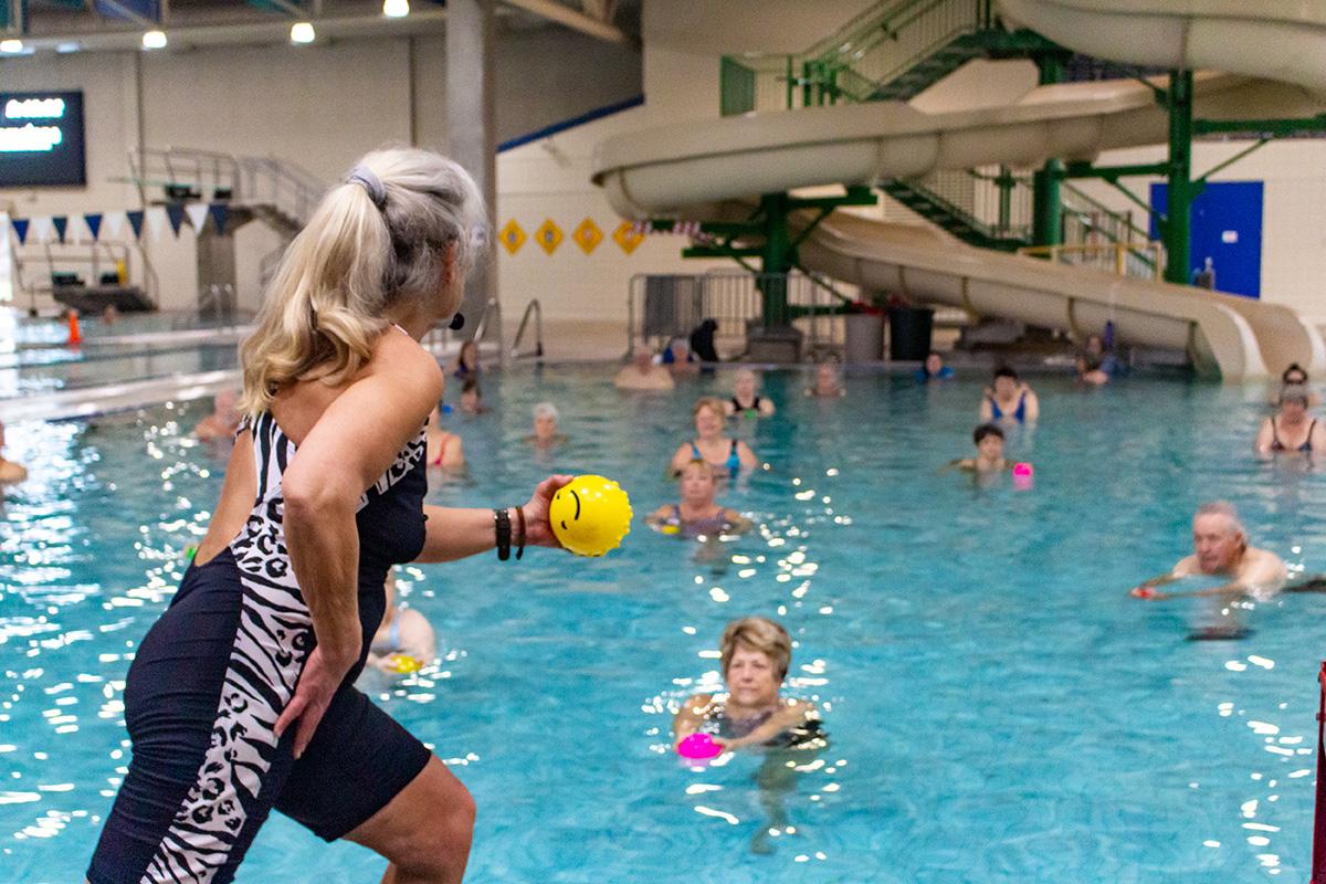Close up of water fitness instructor holding a soft ball while her students imitate this movement