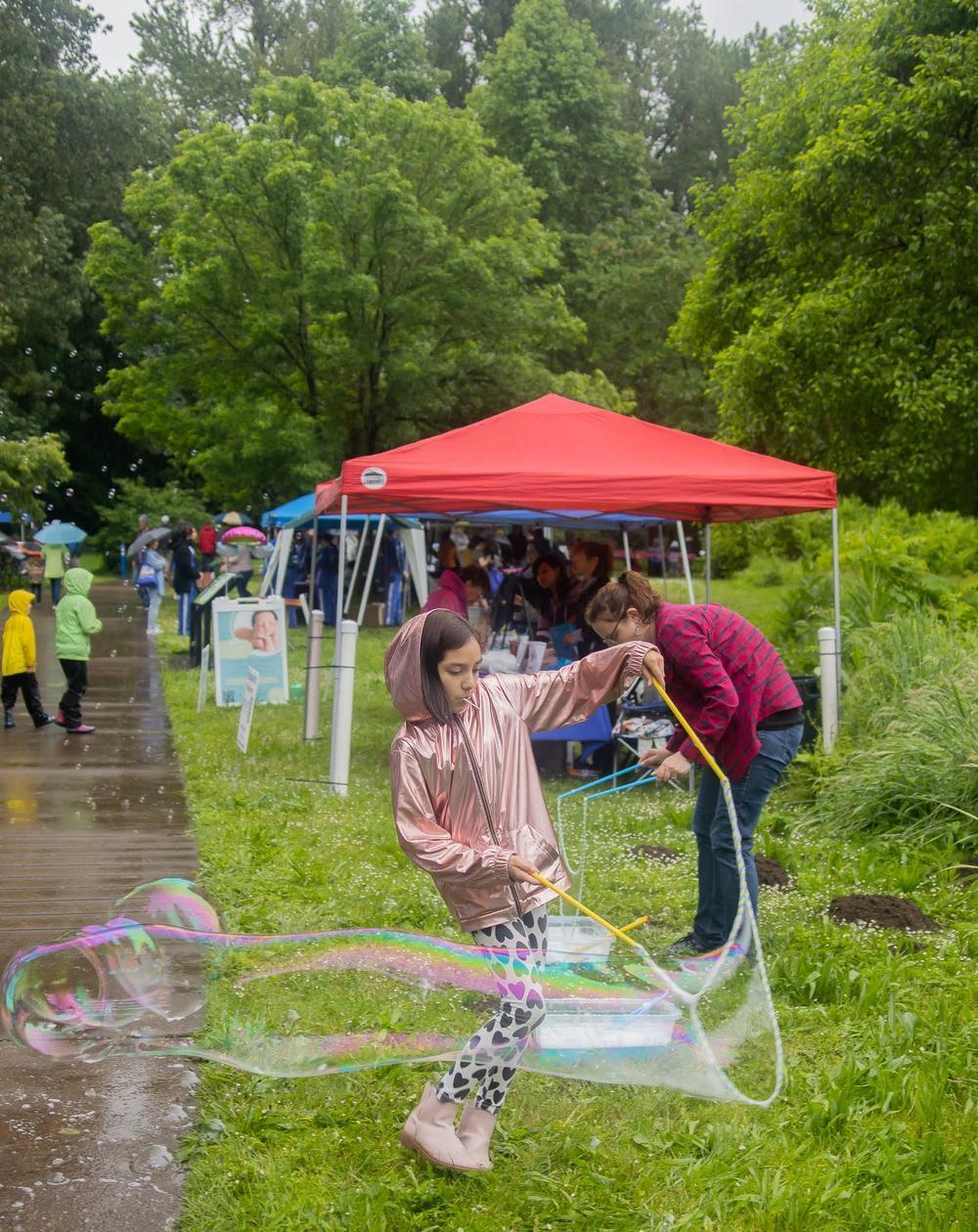 Child makes large bubble at Children's Celebration in the rain