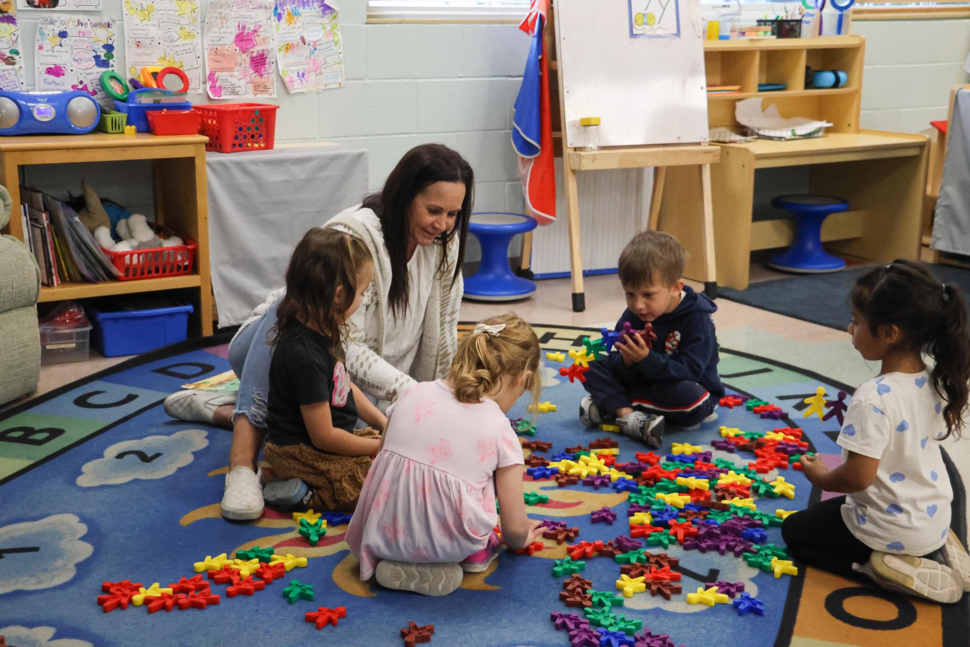 A teacher sits on the floor doing an activity with students.