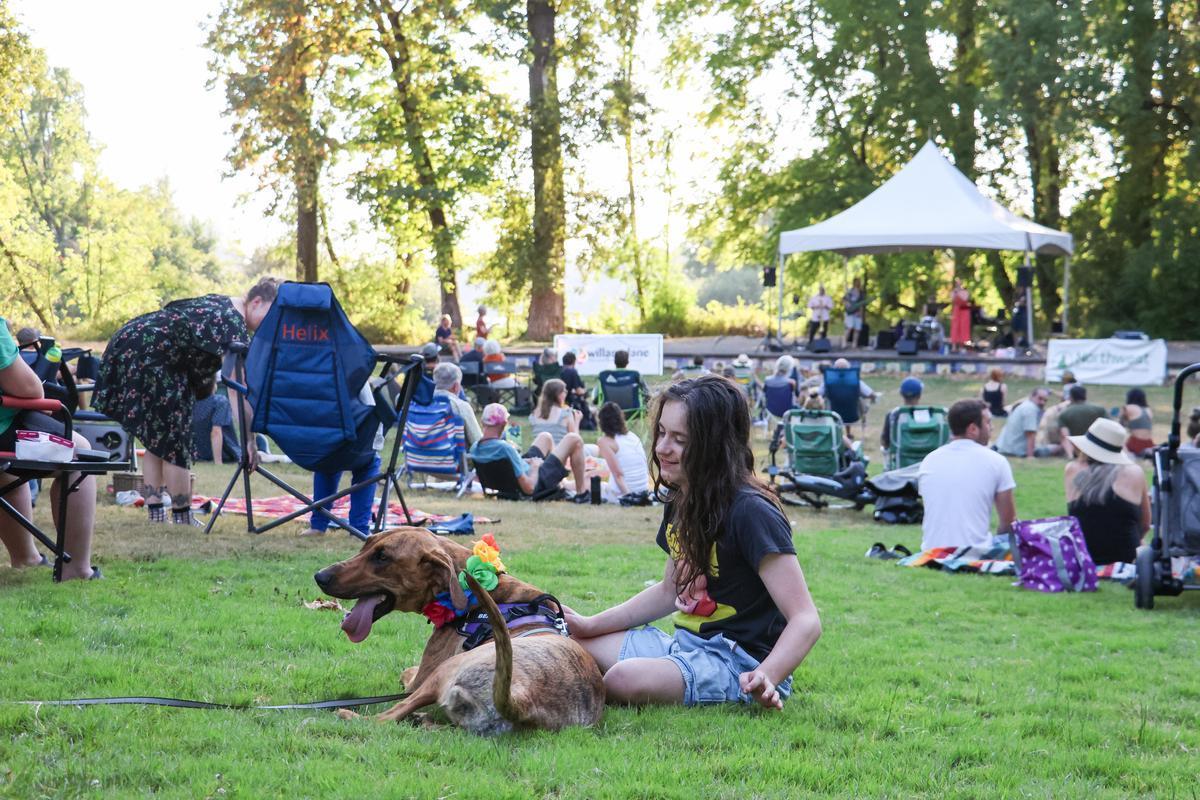 A person and their dog sit on the Island Park grass.