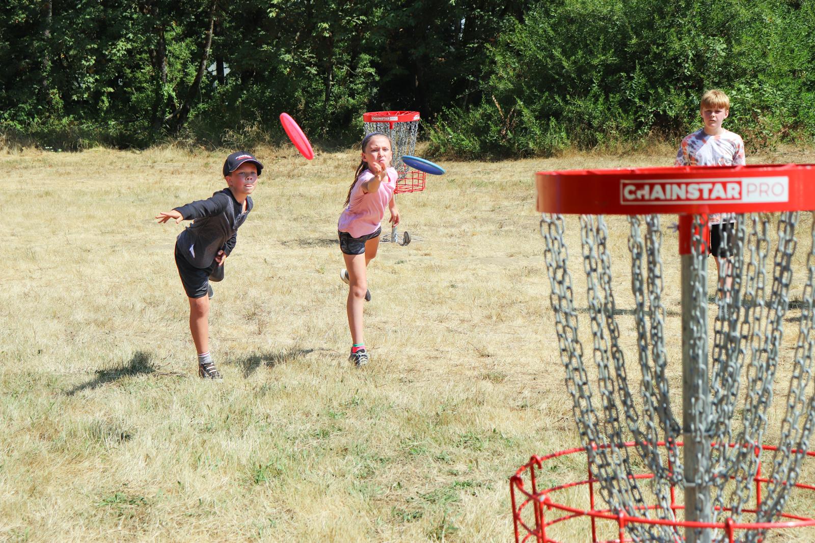 Kids throw discs towards the basket playing disc golf at Clearwater Park